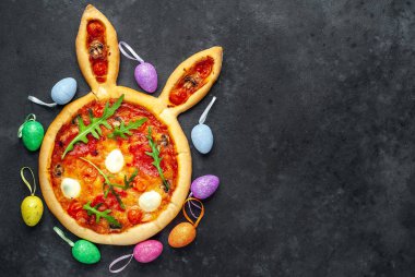 Yumurtalı tavşan şeklinde bayramlık Paskalya pizzası. Taş zeminde çok renkli Paskalya yumurtaları. Paskalya kutlaması kavramı.
