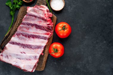 Domatesli çiğ domuz pirzolası, otlar ve baharatlar koyu arka planda.