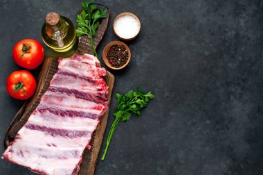 Domatesli çiğ domuz pirzolası, otlar ve baharatlar koyu arka planda.