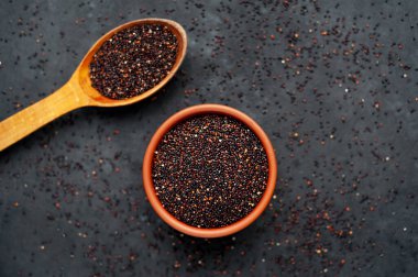 Ahşap kaşıkta kırmızı kinoa tohumları ve koyu arkaplanda kase