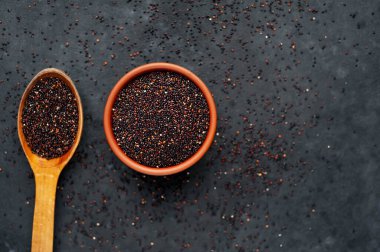 Ahşap kaşıkta kırmızı kinoa tohumları ve koyu arkaplanda kase