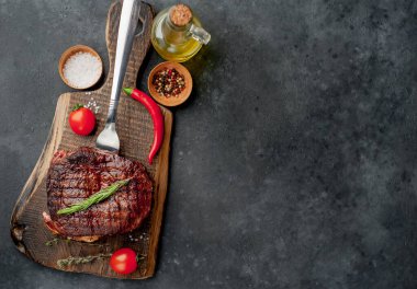 Baharatlı ızgara biftek, domates ve siyah arka planda otlar.