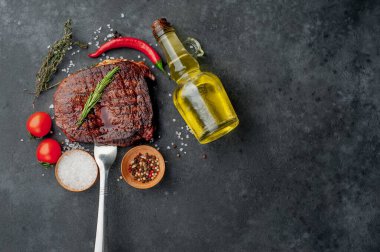 Baharatlı ızgara biftek, domates ve siyah arka planda otlar.