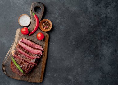 Baharatlı ızgara biftek, domates ve siyah arka planda otlar.