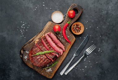 Baharatlı ızgara biftek, domates ve siyah arka planda otlar.