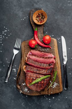 Baharatlı ızgara biftek, domates ve siyah arka planda otlar.