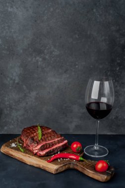 Bir bardak kırmızı şarap ve siyah bir arka planda biftek.