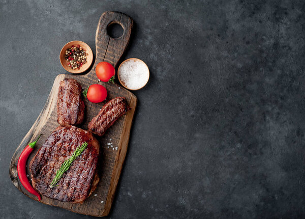 grilled beef steak with spices, tomatoes and herbs on dark background. top view. free space for text.