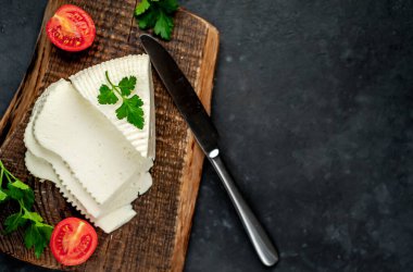 Beyaz inek peyniri üçgeni domatesli dilimler ve ahşap tahta üzerinde ahşap masa arka planında yeşiller