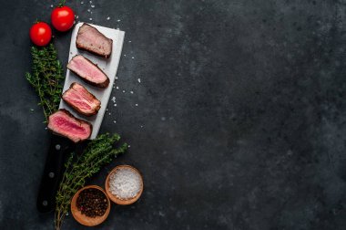 Orta az pişmiş, otlu biftek dilimleri ve gri kırsal masa arka planında biberiye dalları.