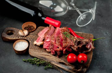 Kırsal masada ızgara biftek dilimleri ve kırmızı şarap bardakları.