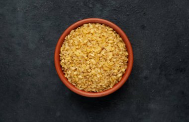 Pişmemiş çiğ bulgur taneleri gri kırsal masa arka planında. 