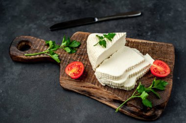 Beyaz inek peyniri üçgeni domatesli dilimler ve ahşap tahta üzerinde ahşap masa arka planında yeşiller