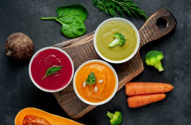 Kabak, havuç ve brokoli dolu kremalı kaseler kırsal masa arkasında.