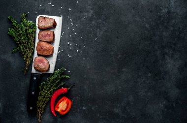 Bitkilerle ve biberiye dallarıyla dilimlenmiş madalyon bifteği.