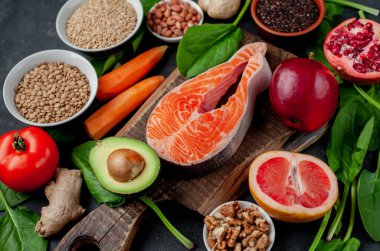 Kırmızı somon balıklı keto diyeti, taze farklı sebzeler ve meyveler, fındık ve kırsal masa arka planında yeşiller