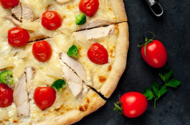 Ev yapımı pizza dilimleri, arka planda tavuk eti, peynir ve domates.