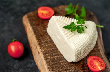 Beyaz inek peyniri üçgeni domatesli dilimler ve ahşap tahta üzerinde ahşap masa arka planında yeşiller