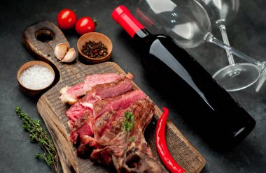 Kırsal masada ızgara biftek dilimleri ve kırmızı şarap bardakları.