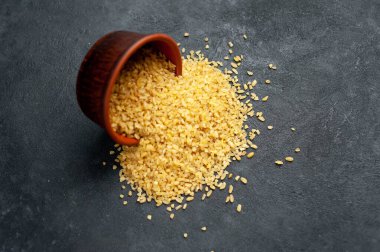 Pişmemiş çiğ bulgur taneleri gri kırsal masa arka planında. 