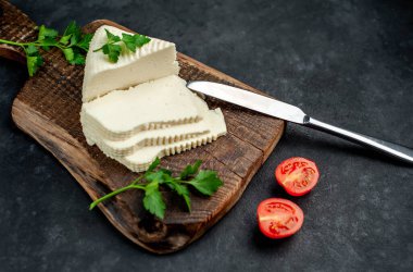 Beyaz inek peyniri üçgeni domatesli dilimler ve ahşap tahta üzerinde ahşap masa arka planında yeşiller