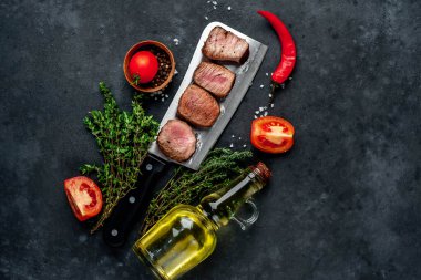Lezzetli ızgara biftek parçaları otlar ve zeytinyağı şişeli domatesler kırsal masa arkasında.