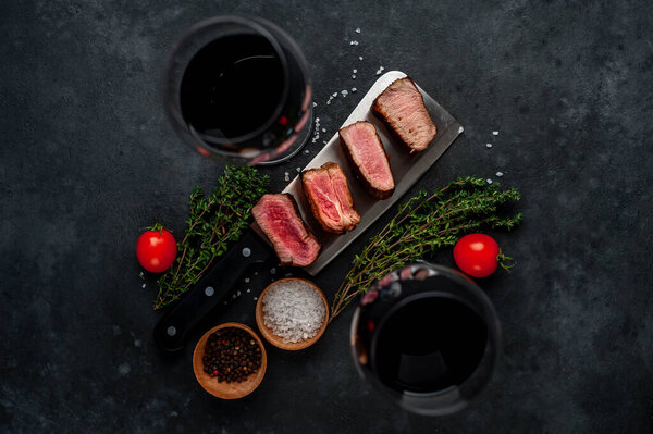 grilled medium rare medallion steak slices with herbs and wine glasses on gray rustic table background