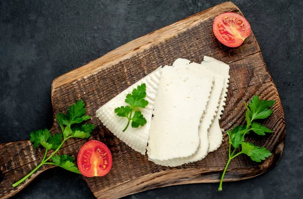 white cow feta cheese triangle slices with tomatoes and greens on wooden board on rustic table background