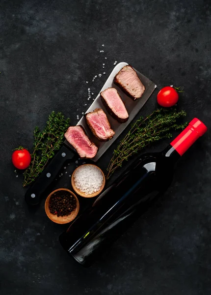 ジューシーなグリルメダイヨンステーキ肉スライスハーブと赤ワインボトル素朴なテーブルの背景に — ストック写真