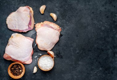 Çiğ tavuk butları ve arka planda baharatlar olan et bıçağı.