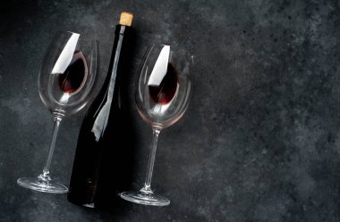 Kırmızı şarap şişesi ve taş bir arka planda gözlük.