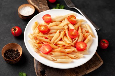 Domates soslu makarna ve arka planda beyaz bir tabakta ızgara tavuk budu.