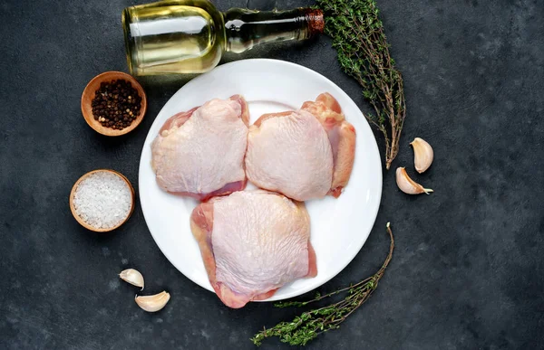 Raw chicken thighs and meat knife with spices on a stone background