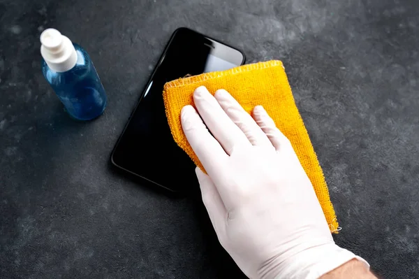 male hand in a medical glove wipes the phone with alcohol, prevents infection with the Covid-19 virus.