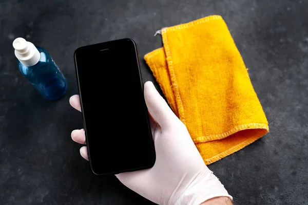 male hand in a medical glove wipes the phone with alcohol, prevents infection with the Covid-19 virus.