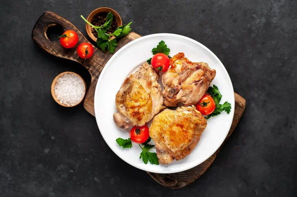 Grilled chicken thighs on a cutting board with spices on a stone background with copy space for your text