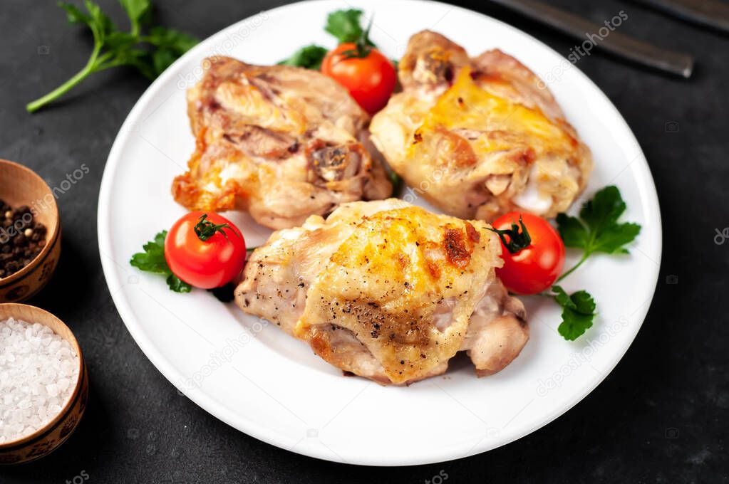 Grilled chicken thighs on white plate with spices on a stone background with copy space for your text