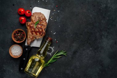 Koyu bir arka planda ızgara kaburga eti ve yağ şişesi.