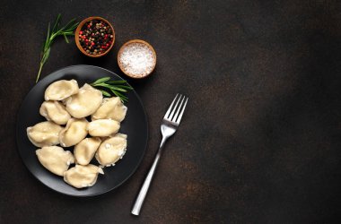 Koyu masa yüzeyinde pierogi köftesi ve çatal tabağı.