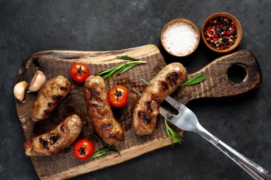 Metnin için fotokopi alanı olan taştan bir arka plandaki kesme tahtasındaki malzemelerle ızgara sosisler.