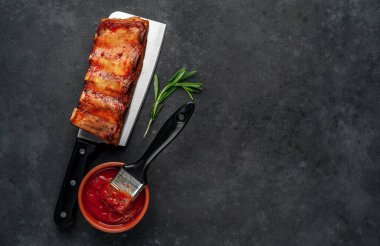 Mutfak baltasında domuz kaburgası ve siyah masada bitki ve ketçap.