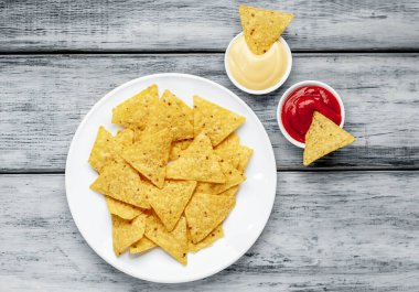 Tahta masa arkasında üçgen şekilli mısır tortilla cipsi ve soslu tabak, yakın görüş. 