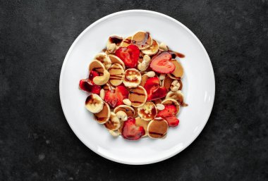 Çilekli mini krepler, muzlar, arka planda bir tabakta fındıklar. Nefis kahvaltı konsepti