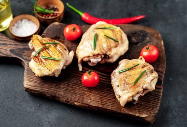 Fırında tavuk butları ahşap kesme tahtasında domates ve baharatlarla, yakın görüş 