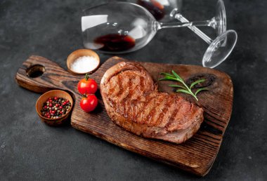 Kesme tahtasında baharatlı ızgara biftek ve arka planda gözlük.