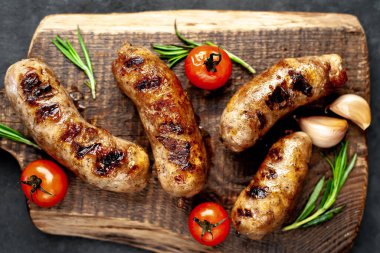 Kızarmış sosisler ve malzemeler taştan bir arka planda kesim tahtasının üzerinde.