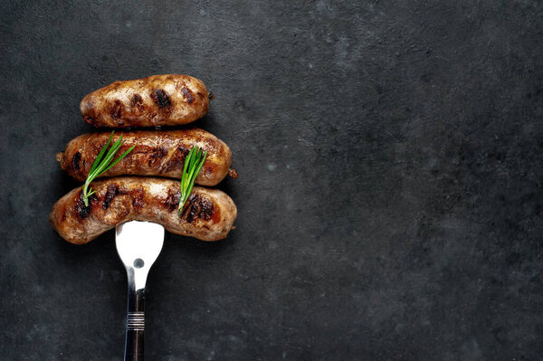 grilled sausages on a meat fork on a stone background with copy space for your text