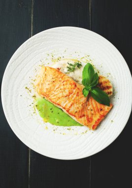 Sos ve baharatlı fırında somon. Beyaz bir tabakta. Koyu bir sırtüstü.