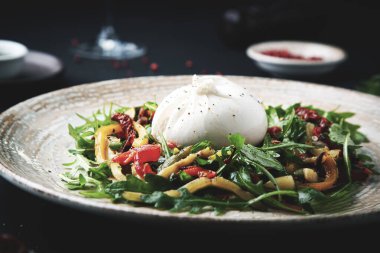 Burrata, roka, marul ve koyu arkaplanda kurutulmuş domatesli taze salata.