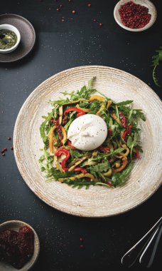 Burrata, roka, marul ve koyu arkaplanda kurutulmuş domatesli taze salata.
